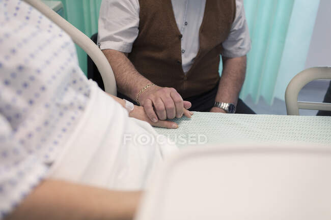 Affectionate senior man holding hands with wife resting in hospital bed — Stock Photo