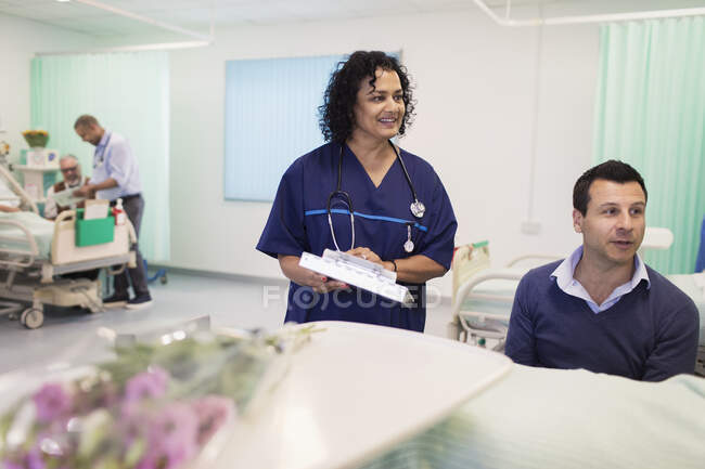 Médico con historial médico haciendo rondas en la sala del hospital - foto de stock