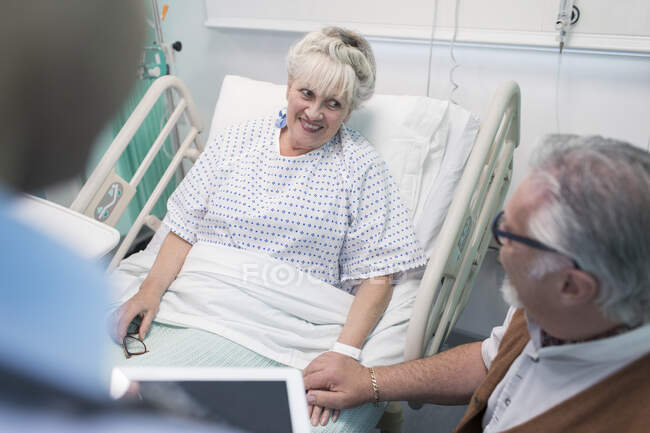 Homem idoso afetuoso conversando com a esposa descansando na cama do hospital — Fotografia de Stock