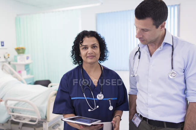 Portrait confident doctors with digital tablet making rounds, consulting in hospital room — Stock Photo