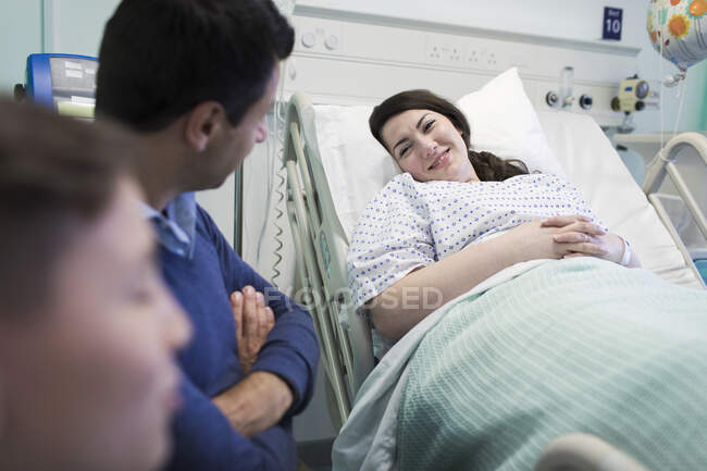Сім'я, яка відвідує усміхненого пацієнта, відпочиває в лікарняному ліжку — стокове фото