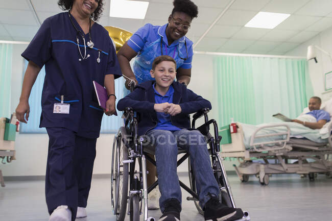 Médecin et infirmière poussant garçon patient en fauteuil roulant dans la salle d'hôpital — Photo de stock