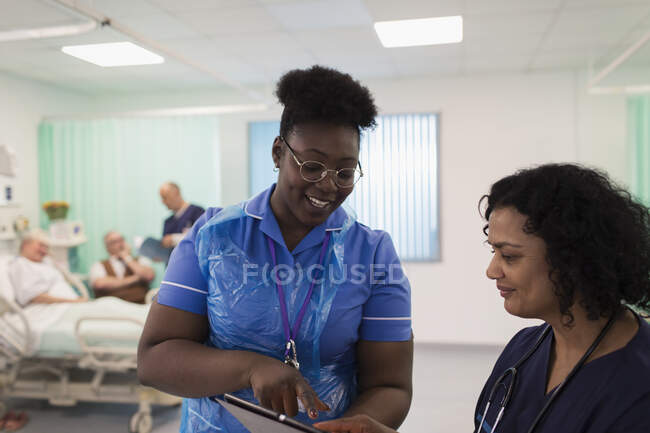 Doctora y enfermera con tableta digital haciendo rondas, consultando en habitación de hospital - foto de stock