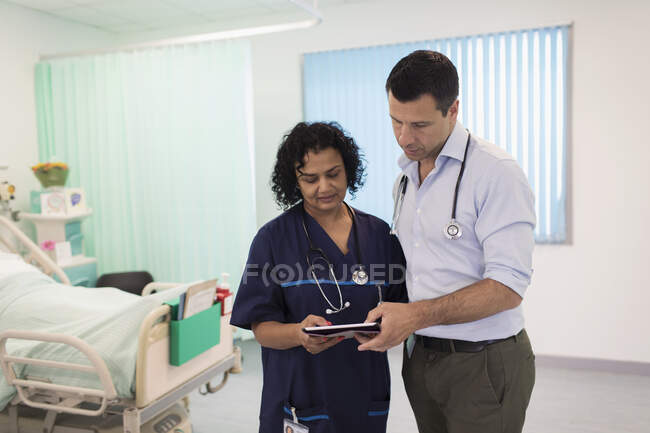 Лікарі з цифровим планшетом роблять раунди, консультування в лікарняній кімнаті — стокове фото