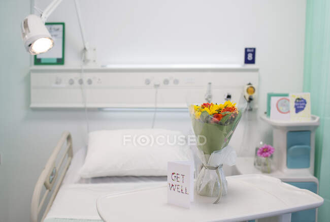 Flower bouquet and Get Well greeting card on tray in vacant hospital room — Stock Photo