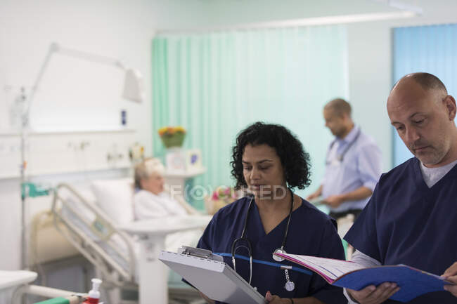 Médicos con historias clínicas haciendo rondas, consultoría en habitación de hospital - foto de stock