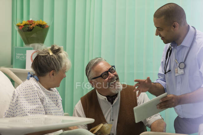 Médico com tablet digital fazendo rondas, conversando com casal de idosos no quarto do hospital — Fotografia de Stock
