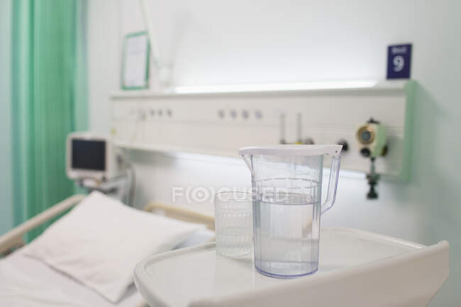 Brocca d'acqua e vetro sul vassoio nella stanza d'ospedale vuota — Foto stock