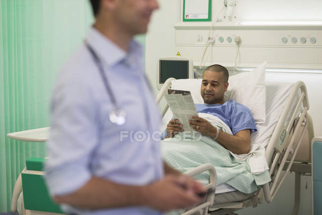 Hombre leyendo el periódico, descansando en la habitación del hospital - foto de stock