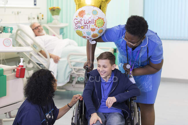 Лікар і медсестра розмовляють з пацієнтом-хлопчиком у інвалідному візку в лікарняному відділенні — стокове фото