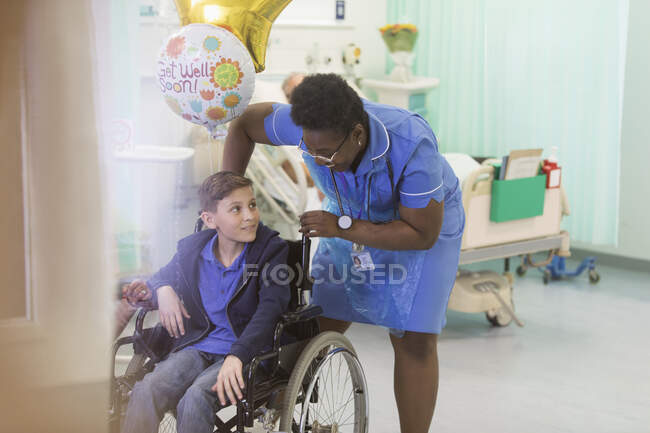 Enfermeira empurrando menino paciente em cadeira de rodas no quarto do hospital — Fotografia de Stock