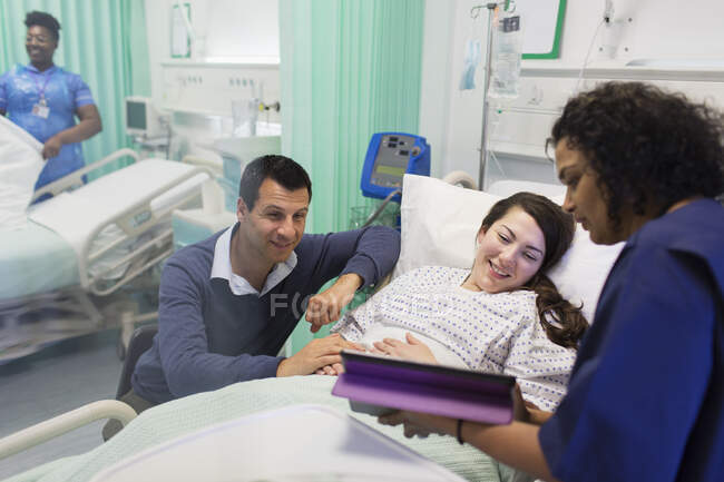 Doctor con tableta digital haciendo rondas, hablando con pareja en la sala de hospital - foto de stock