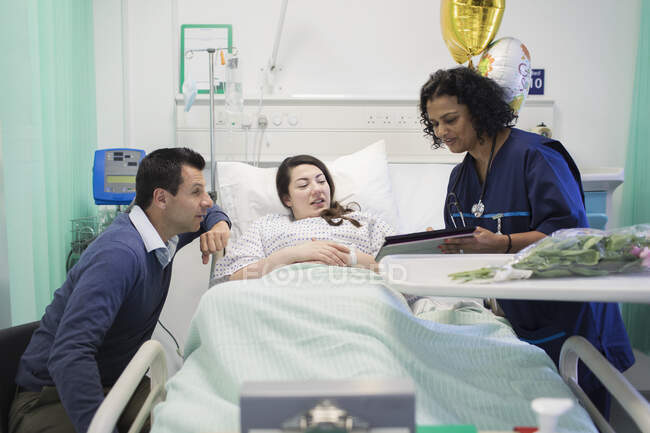 Doctor con tableta digital haciendo rondas, hablando con pareja en habitación de hospital - foto de stock