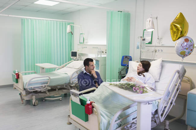 Hombre visitando, hablando con su esposa descansando en el hospital - foto de stock