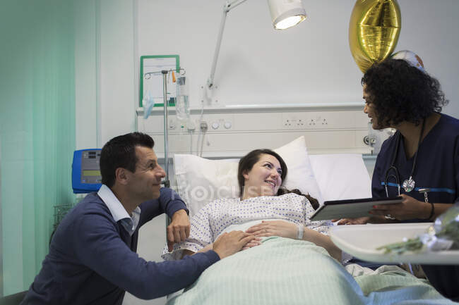 Врач с цифровыми планшетами делает обходы, разговаривает с парой в больничной палате — стоковое фото