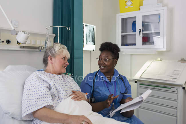 Female nurse talking with senior patient in hospital room — Stock Photo