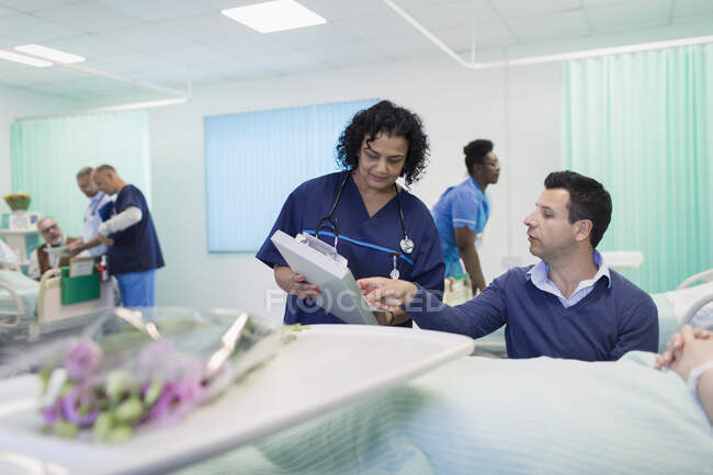 Лікар з медичною картою робить раунди, розмовляє з відвідувачем лікарні — стокове фото
