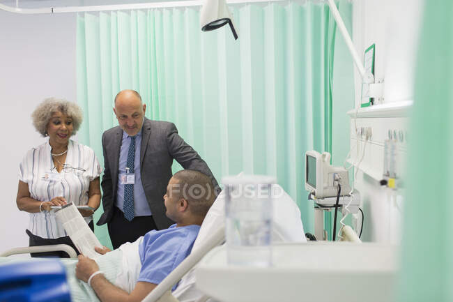 Médecins faisant des rondes, parlant avec le patient lisant le journal dans la chambre d'hôpital — Photo de stock