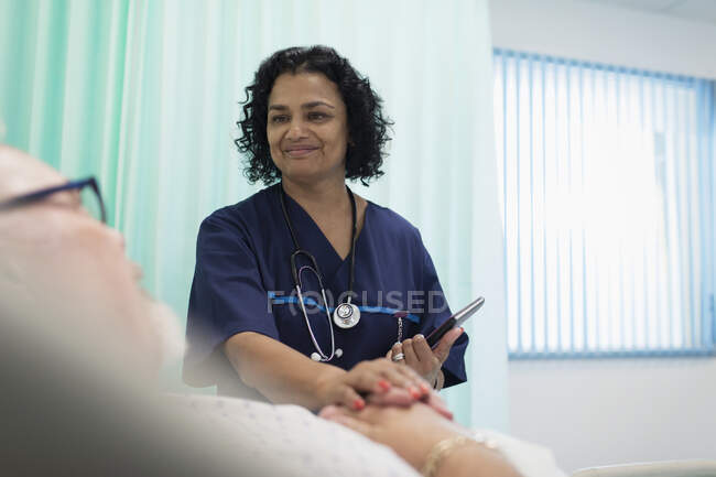 Médico sorridente com tablet digital fazendo rondas, confortando o paciente descansando no quarto do hospital — Fotografia de Stock