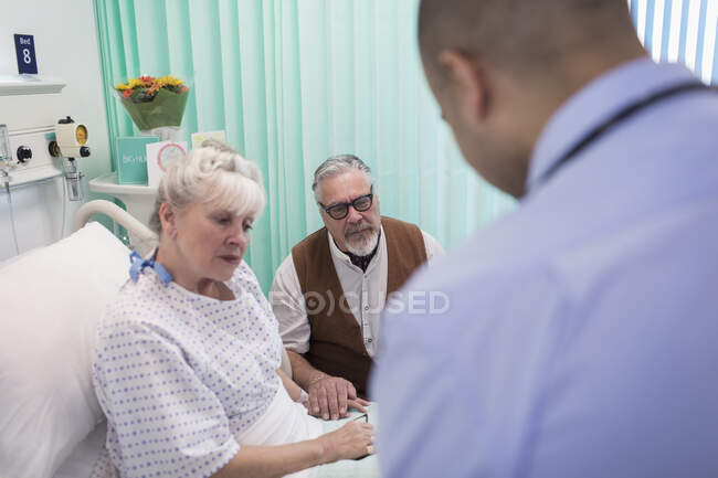 Доктор делает обход, разговаривает с пожилой парой в больничной палате — стоковое фото