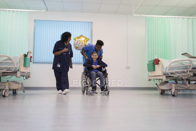 Médecin et infirmière poussant garçon patient en fauteuil roulant dans la salle d'hôpital — Photo de stock