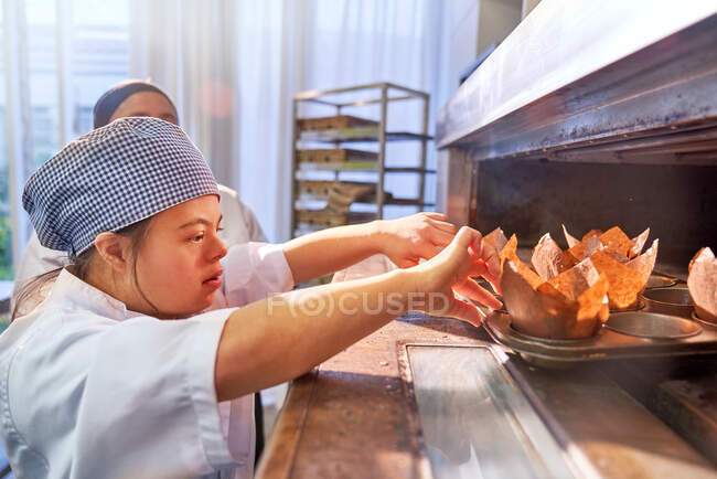Jeune femme trisomique plaçant des muffins au four — Photo de stock