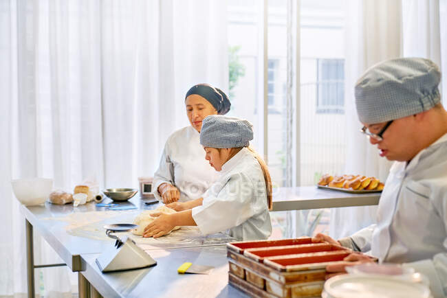 Шеф-повар помогает студентке с синдромом Дауна на кухне — стоковое фото
