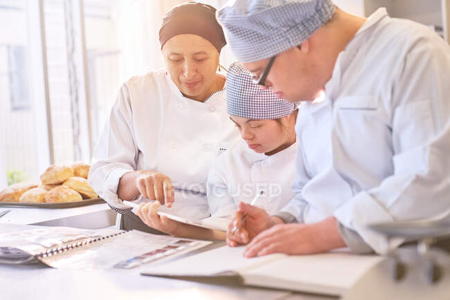 Koch und Studenten mit Down-Syndrom schauen sich Rezepte in der Küche an — Stockfoto