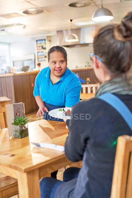 Jovem servidor feminino com síndrome de Down servindo alimentos no café — Fotografia de Stock