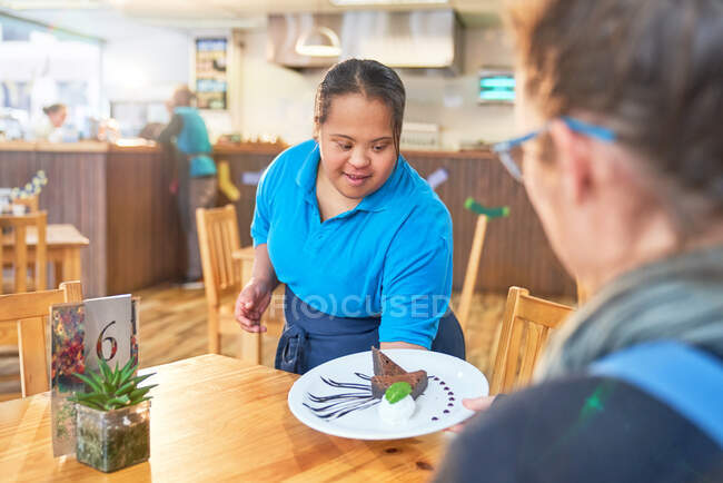 Молода жінка з синдромом Дауна обслуговує десерт у кафе. — стокове фото