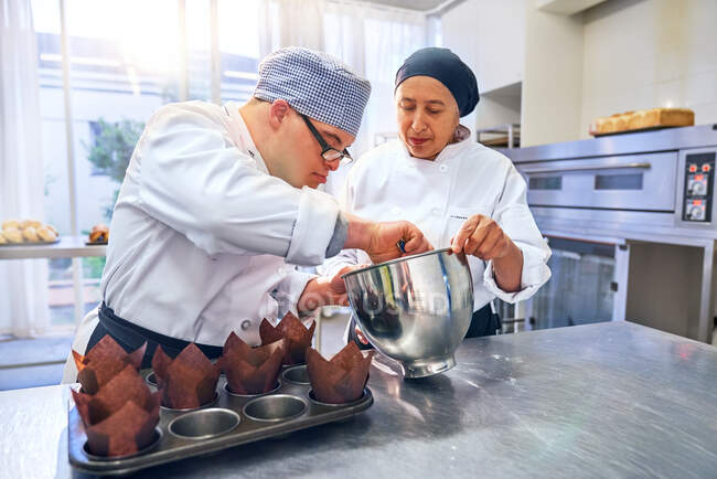 Chef helping student with Down Syndrome baking muffins in kitchen — Stock Photo