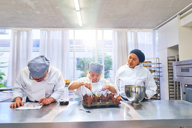 Chef y estudiantes con síndrome de Down hornear magdalenas en la cocina - foto de stock