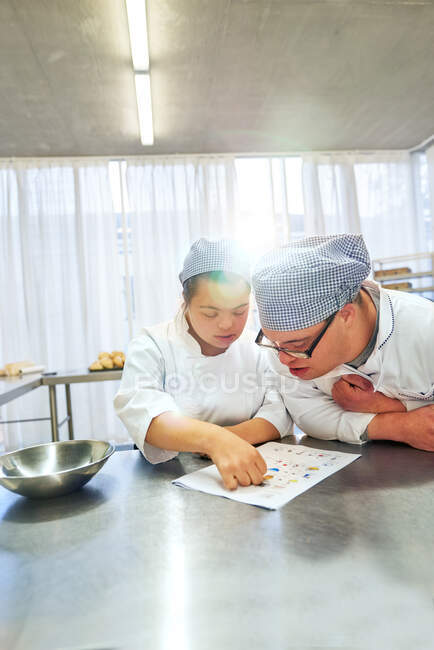 Jóvenes estudiantes con Síndrome de Down mirando la receta en la cocina - foto de stock
