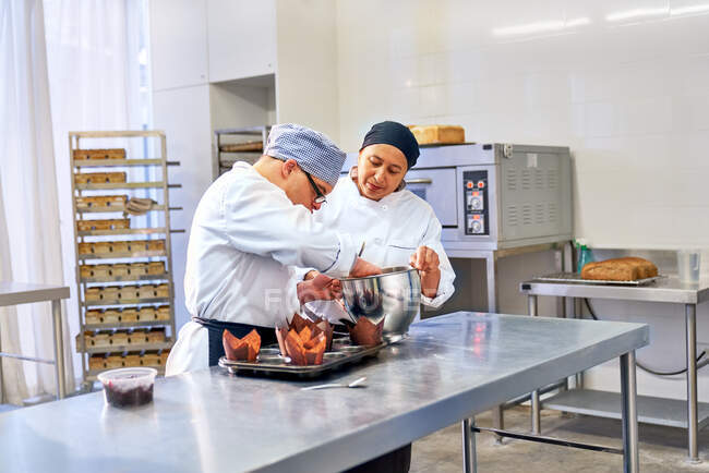 Chef y estudiante con síndrome de Down hornear magdalenas en la cocina - foto de stock