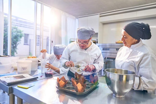 Шеф-кухар допомагає студенту з синдромом Дауна пекти кекси на кухні. — стокове фото