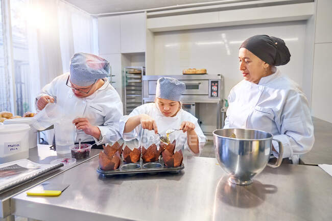 Chef ayudando a estudiantes con Síndrome de Down hornear magdalenas en la cocina - foto de stock