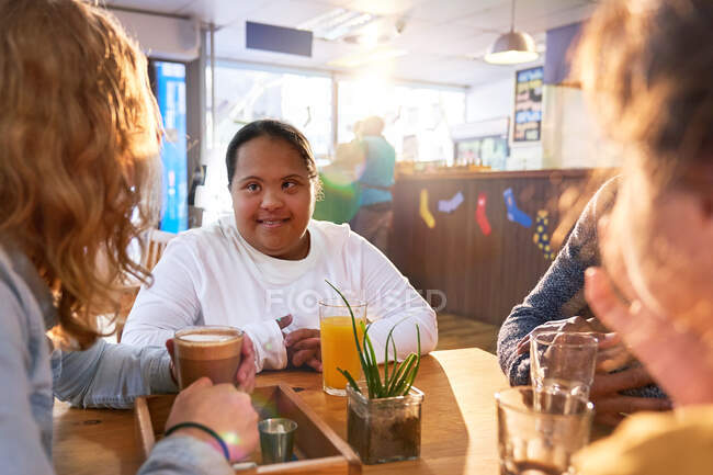 Усміхнена молода жінка з синдромом Дауна розмовляє з друзями в кафе — стокове фото