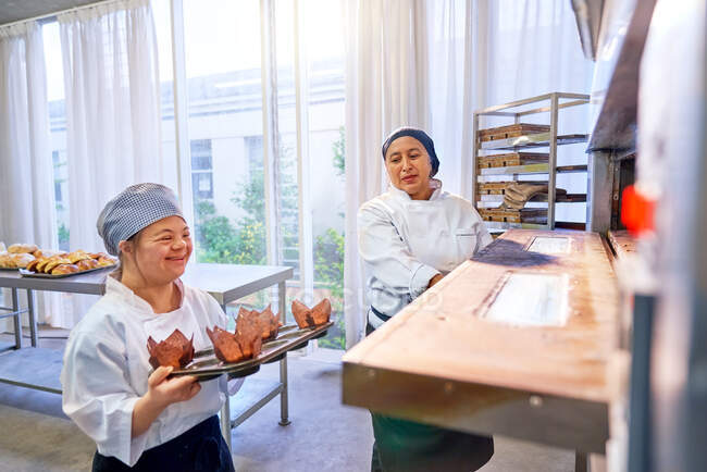Koch und junge Frau mit Down-Syndrom stellen Muffins in den Ofen — Stockfoto