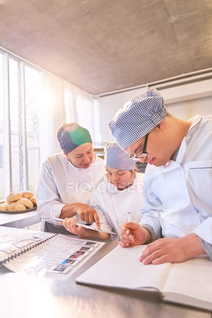 Chef et étudiants atteints de trisomie 21 utilisant une tablette numérique dans la cuisine — Photo de stock