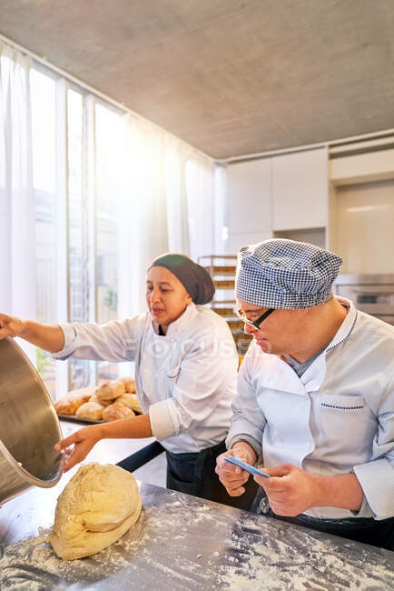 Chef y estudiante con síndrome de Down horneando pan en la cocina - foto de stock