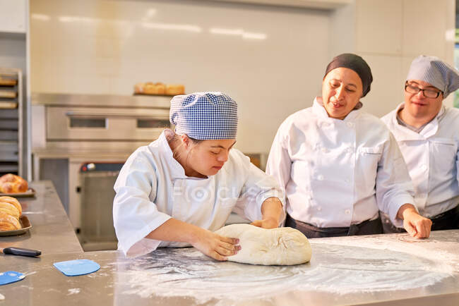 Chef teaching students with Down Syndrome how to knead dough — Stock Photo