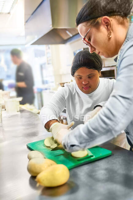 Chef y mujer joven con síndrome de Down cortando papas en la cocina - foto de stock