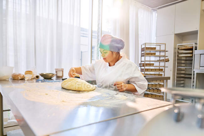Mujer joven con síndrome de Down preparando masa de pan en la cocina - foto de stock