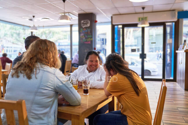 Счастливая молодая женщина с синдромом Дауна в кафе с друзьями — стоковое фото