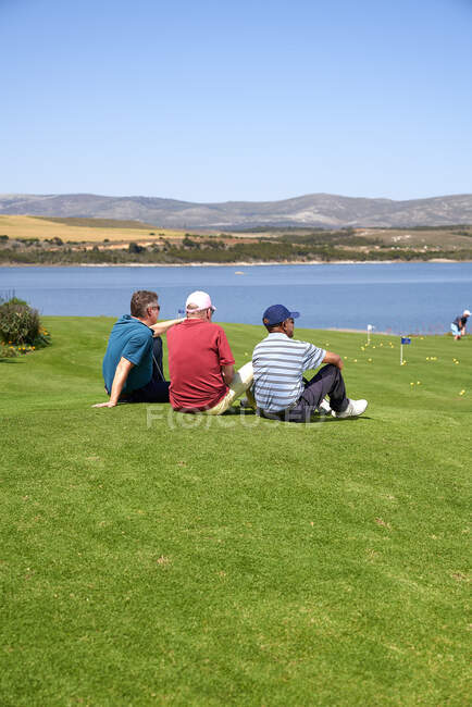 Golfeurs masculins prenant une pause reposant dans l'herbe sur le terrain de golf ensoleillé — Photo de stock