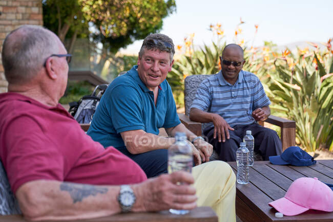 Mature male golfer friends talking and drinking water on patio — Stock Photo