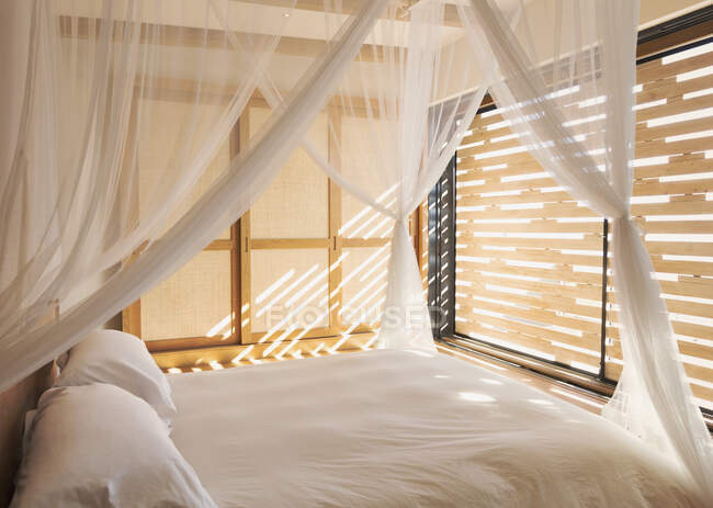 Cortinas de gaze branca na cama dossel em tranquila moderna, casa de luxo vitrine quarto interior — Fotografia de Stock