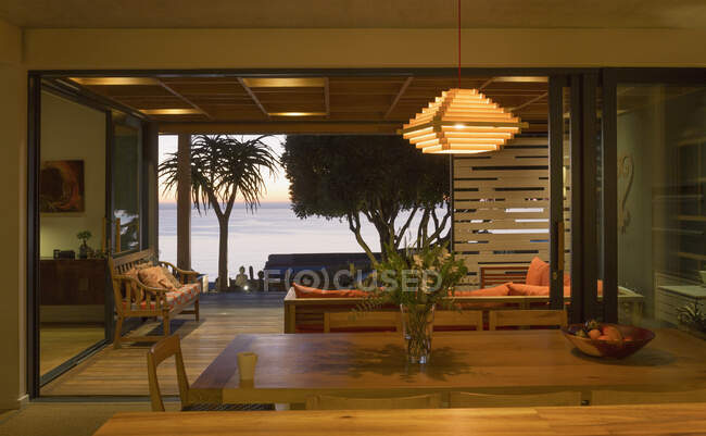 Illuminated modern, luxury home showcase interior dining room open to patio with ocean view — Stock Photo
