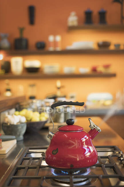 Chaleira de chá vermelho vapor em fogão na cozinha doméstica — Fotografia de Stock