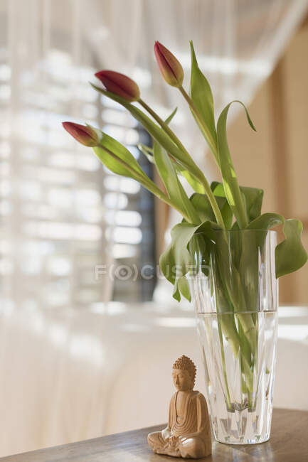 Bouquet Tulip en jarrón y estatua de Buda de madera. - foto de stock